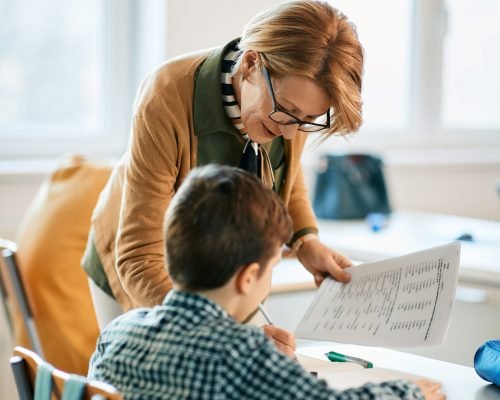 Elementary teacher helping a schoolboy with the lesson in the classroom.
